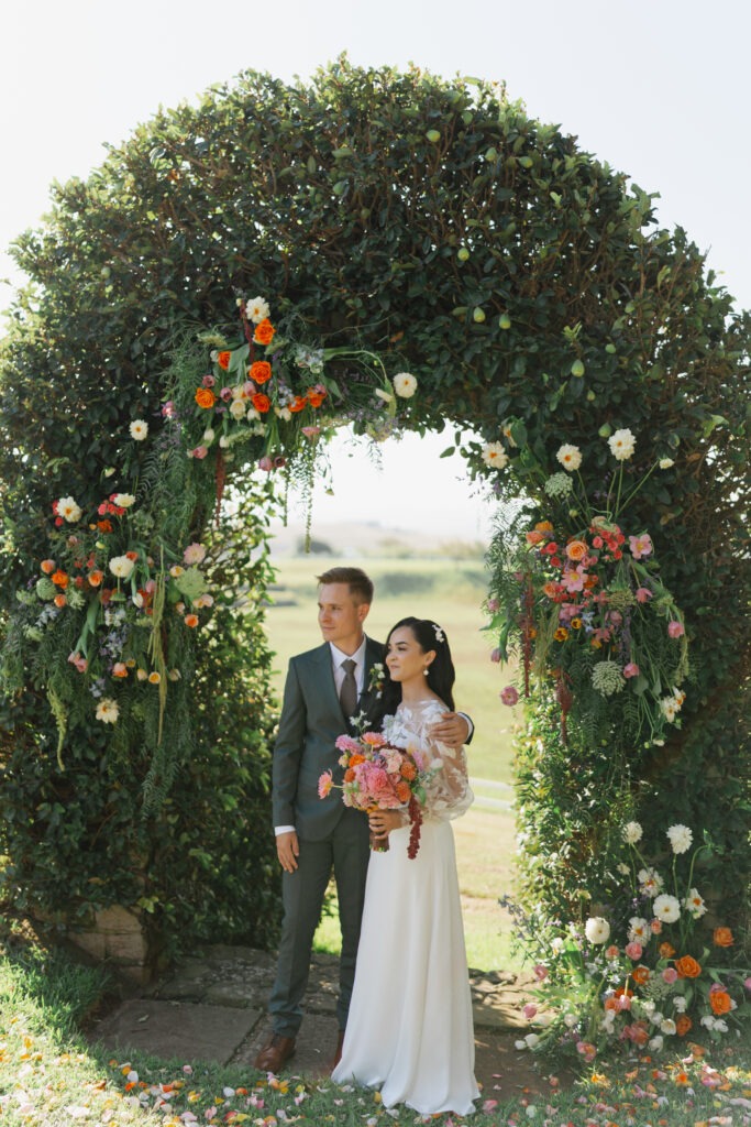 Bride and groom underneath colourful floral arch in Cape Town