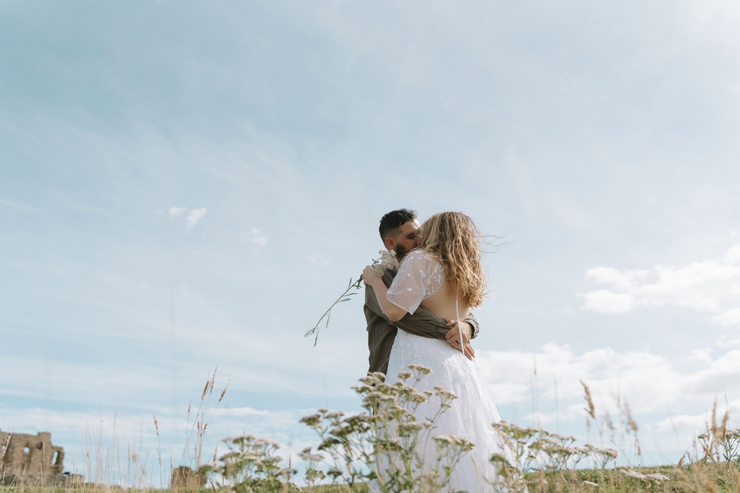 Bride and groom kiss under blue sky in Scotland.