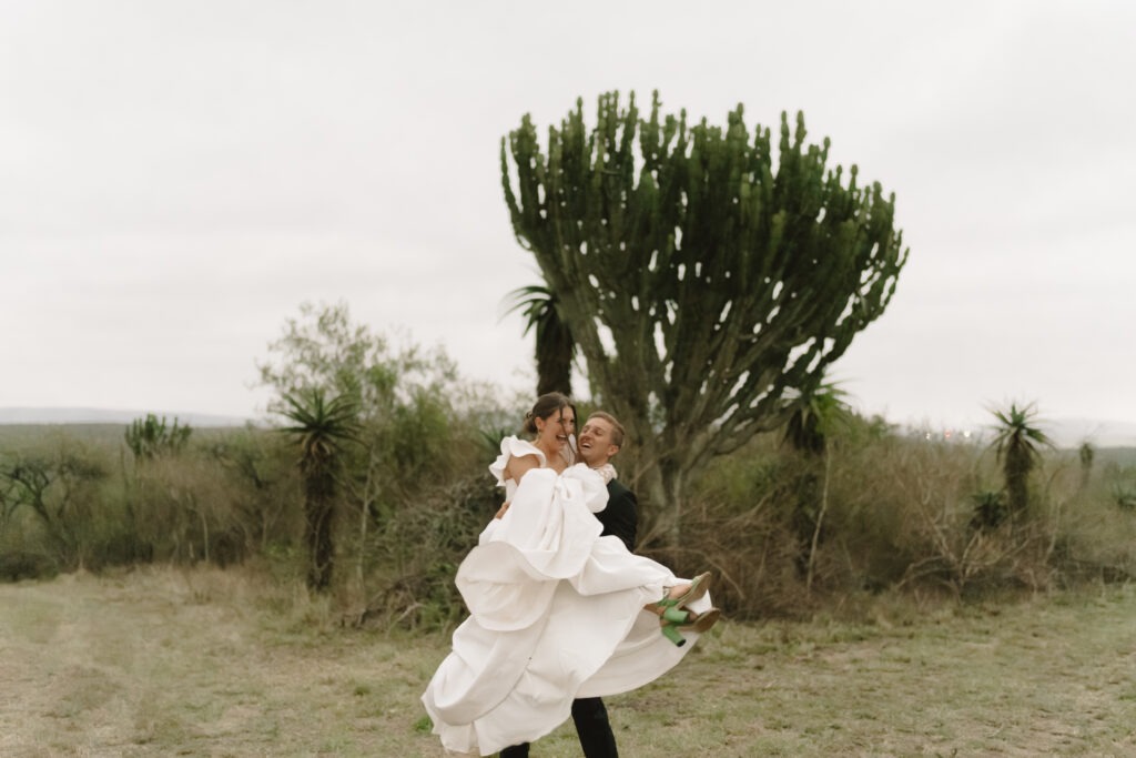 Groom picks up bride underneath cactus tree in South Africa.